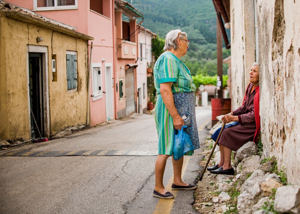 Two elderly ladies chatting to each other on a rustic street in Doukades in Corfu. 