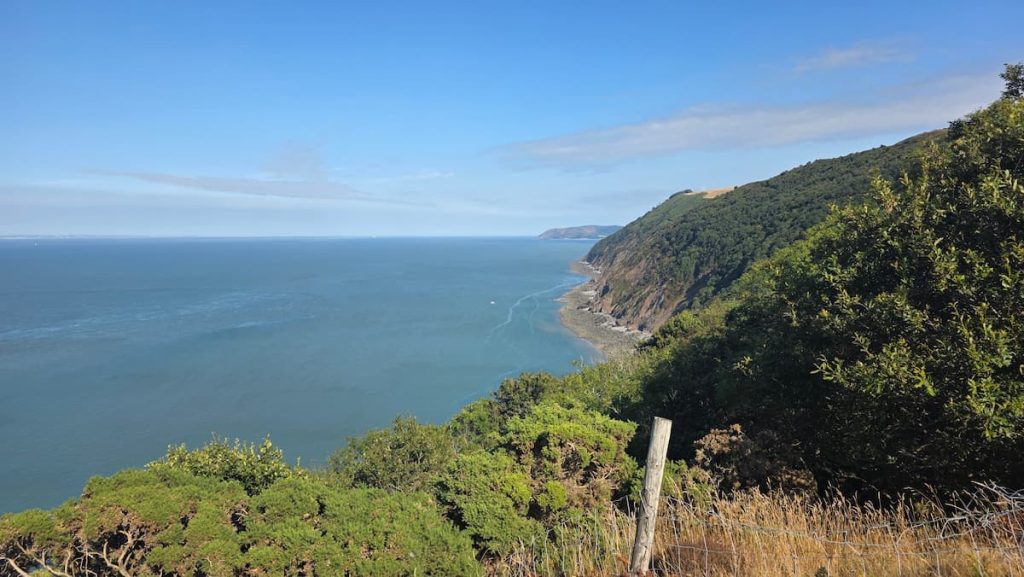 A gorgeous coastal view at Gurney's Wood near Lynmouth overlooking the ocean and the cliff line covered in dense trees on a sunny day.