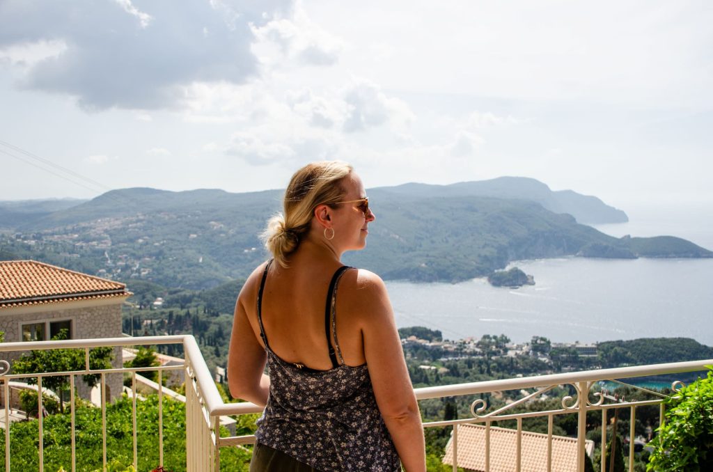 Zara stands at a balcony viewpoint in Lakones, one of the best places to visit for incredibe views of Corfu in October.